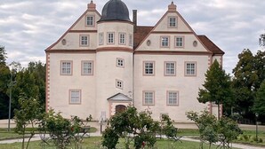 A large, symmetrical building with a central dome and multiple windows, surrounded by a well-maintained lawn and trees. - Hotel Sophienhof (Königs Wusterhausen)