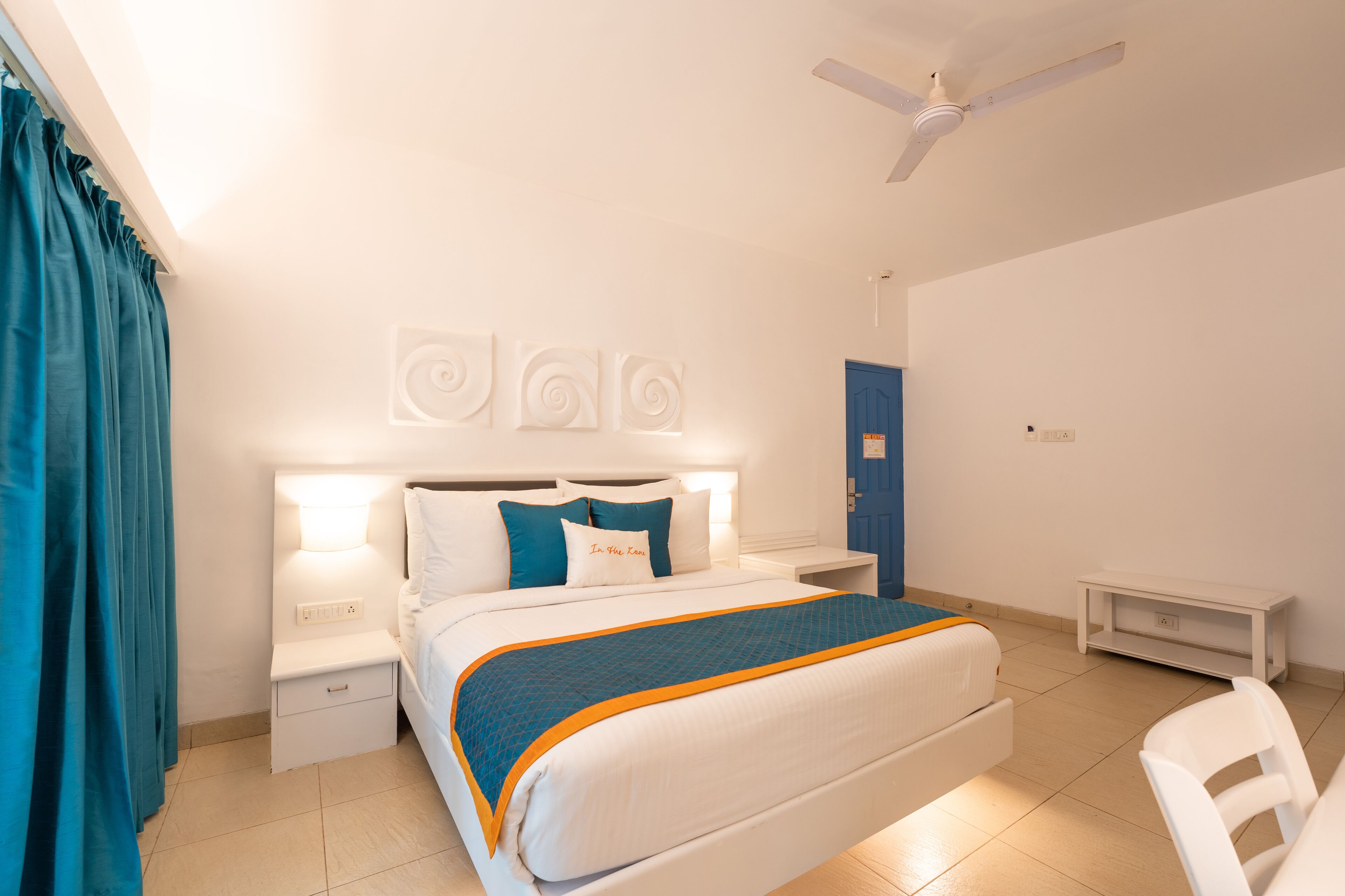 Une chambre d’hôtel équipée d’un lit, de deux tables de chevet, d’un bureau, d’une chaise et d’un ventilateur de plafond.