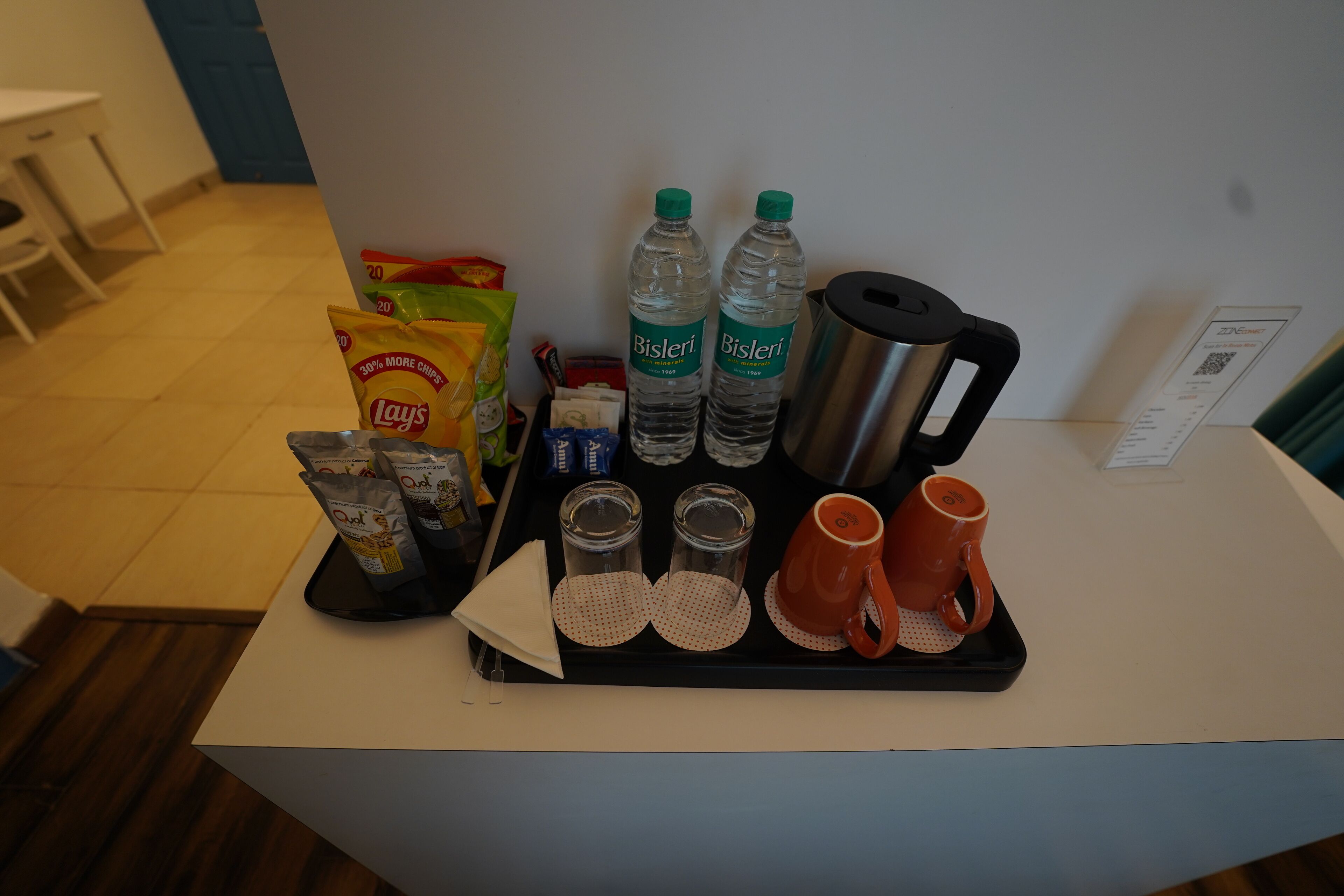 Una bandeja con aperitivos, botellas de agua, una cafetera y tazas sobre una encimera de hotel.