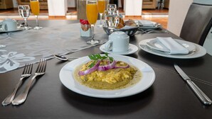 A breakfast setting with a plate of scrambled eggs garnished with red onions and parsley, accompanied by orange juice and water glasses. - Hotel Villa Mexicana Golf Resort (Corregidora)