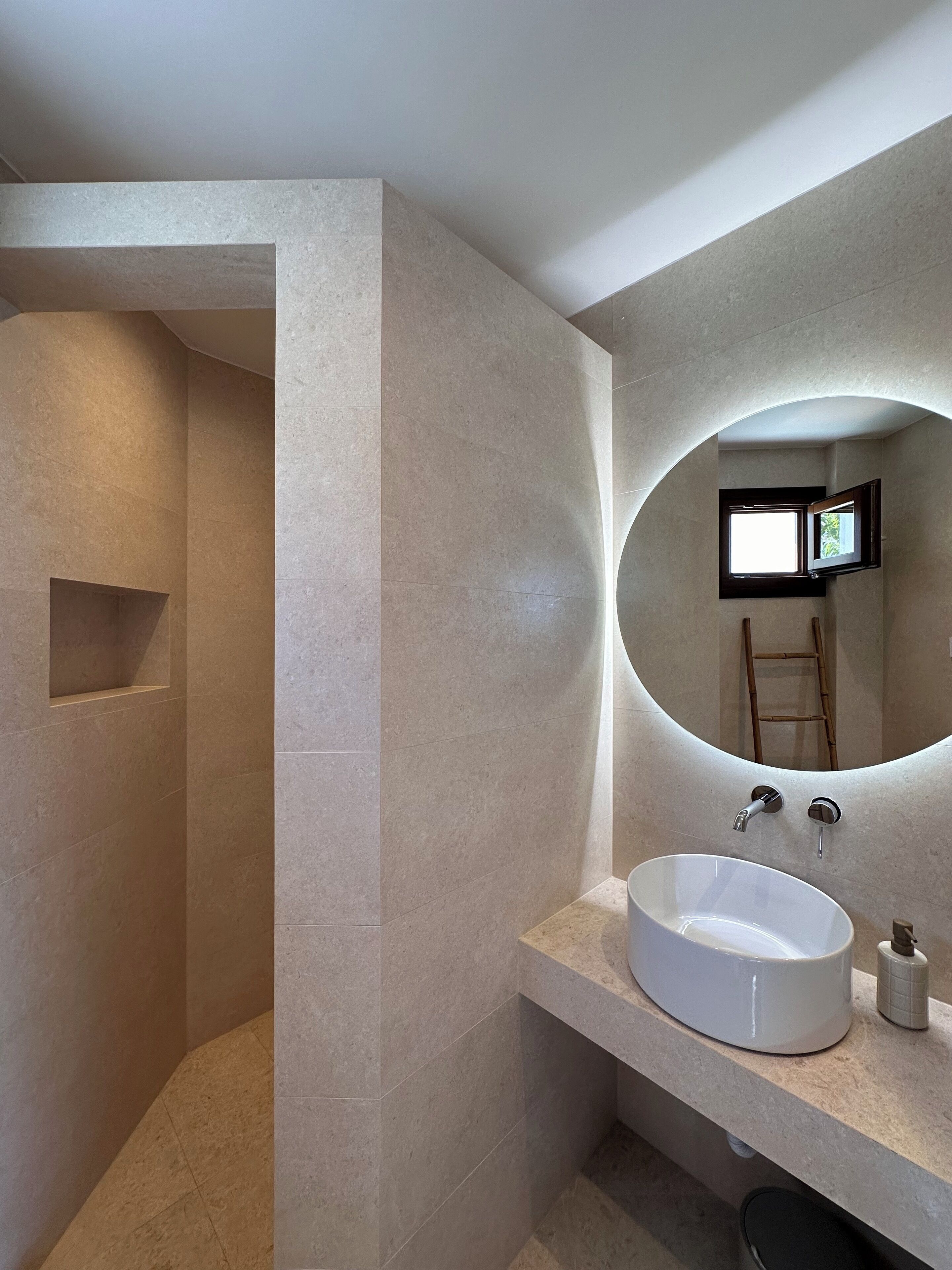 A modern bathroom with a large oval sink, a mirror, and a shower area.