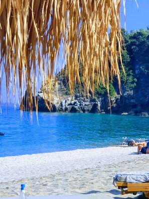 Una playa con agua azul cristalina, un promontorio rocoso y una silla de madera para relajarse.