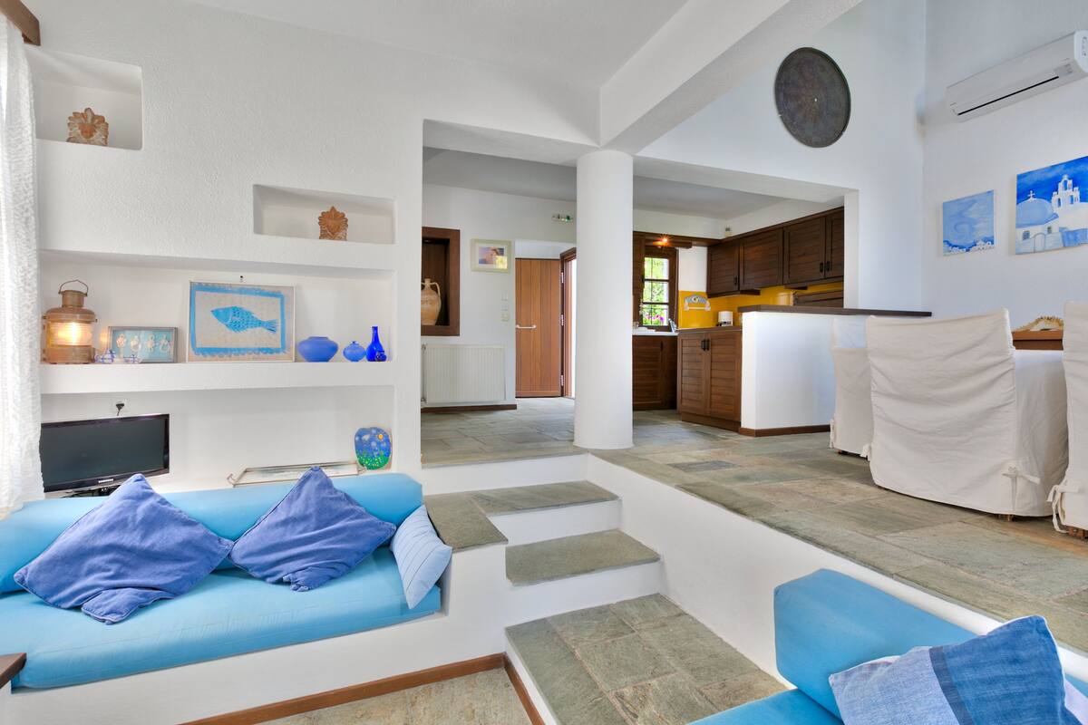 A spacious living area with a blue sofa, a television, and a kitchen in the background.