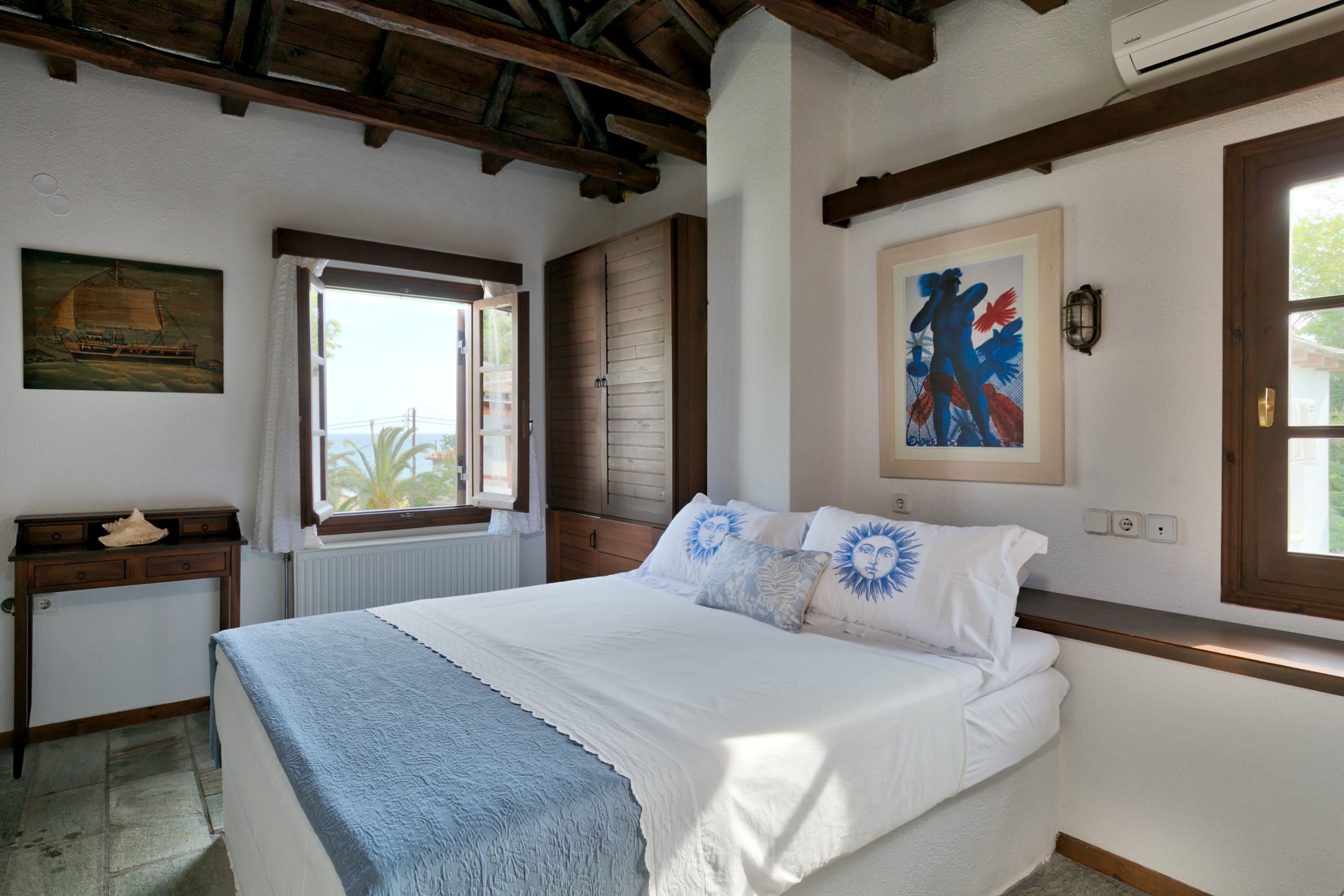 Un dormitorio con una cama grande, una ventana con vistas, un escritorio de madera y un cuadro en la pared.