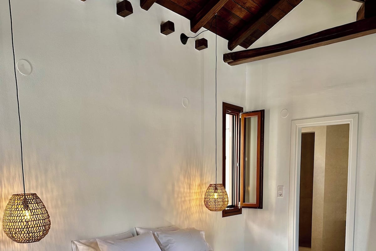 A bedroom with a large bed, a bench, a hanging light fixture, and a mirror on the wall.