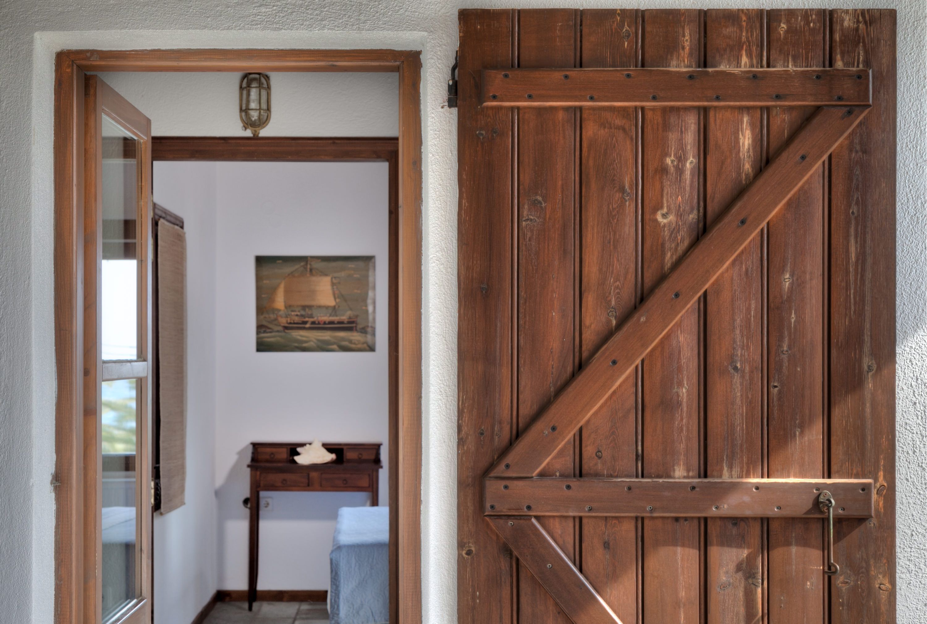 Eine Holztür mit einem Metallriegel, ein kleiner Tisch mit einem weißen Gegenstand darauf und ein Gemälde an der Wand.