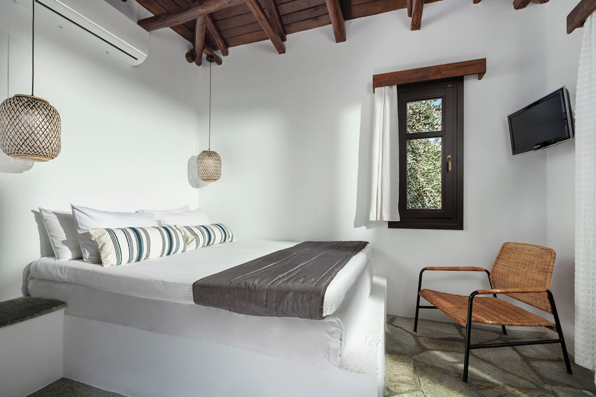 A bedroom with a bed, a chair, a television, and a window.