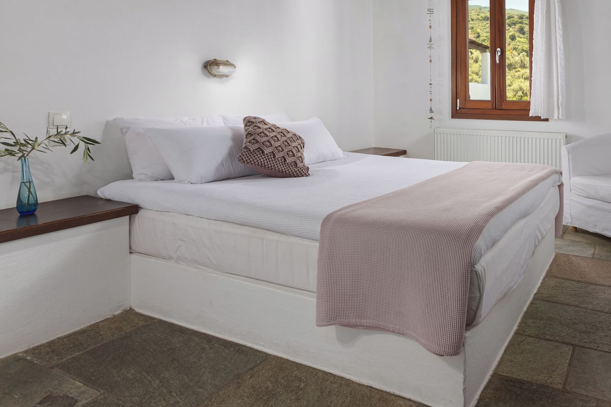A bedroom with a bed, white walls, a wooden ceiling, a window with curtains, and a radiator.