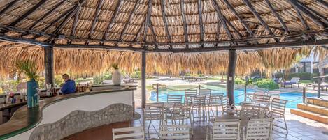 A covered outdoor area with a pool, white metal chairs, and a bar counter.
