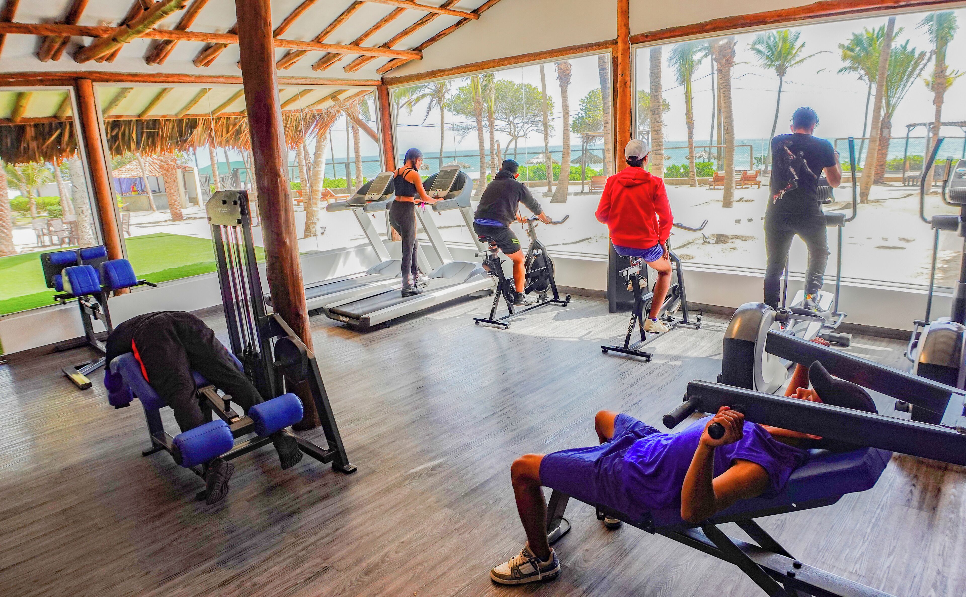 Une salle de sport équipée de machines de cardio, de musculation et offrant une vue sur la plage.