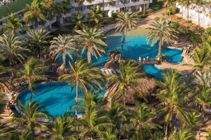 A resort with multiple swimming pools surrounded by palm trees, a bridge, and lounge areas.
