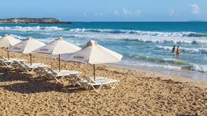 Ein Strand mit weißen Liegestühlen und Sonnenschirmen, einem klaren Himmel und dem Meer.