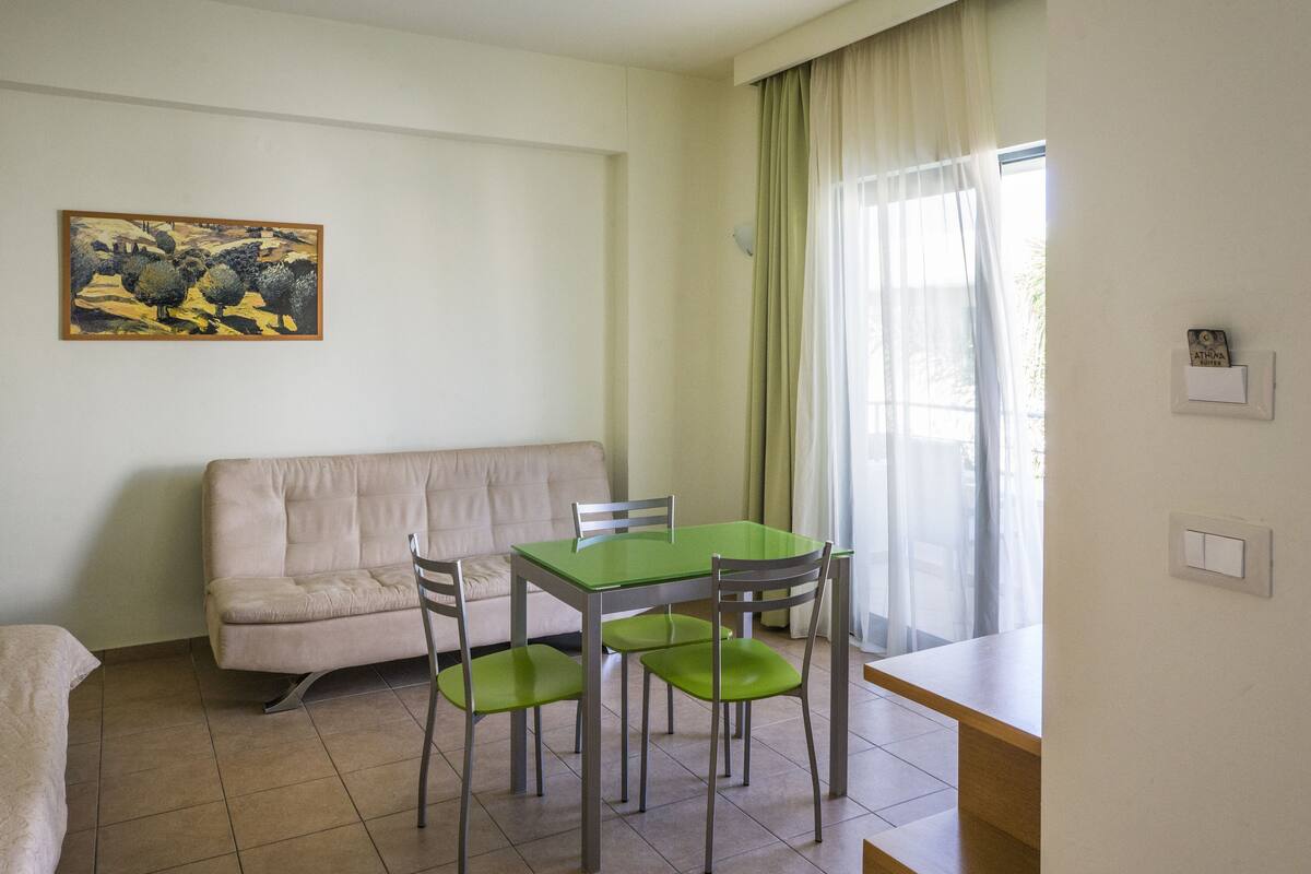 Une pièce avec une table verte et quatre chaises, un canapé beige et un tableau accroché au mur.
