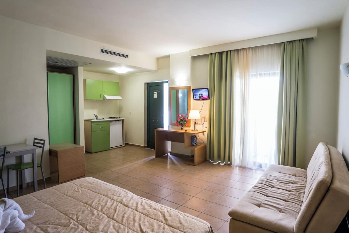 Une chambre d’hôtel comprenant un lit, un canapé, un bureau avec une chaise, une petite kitchenette et un téléviseur.