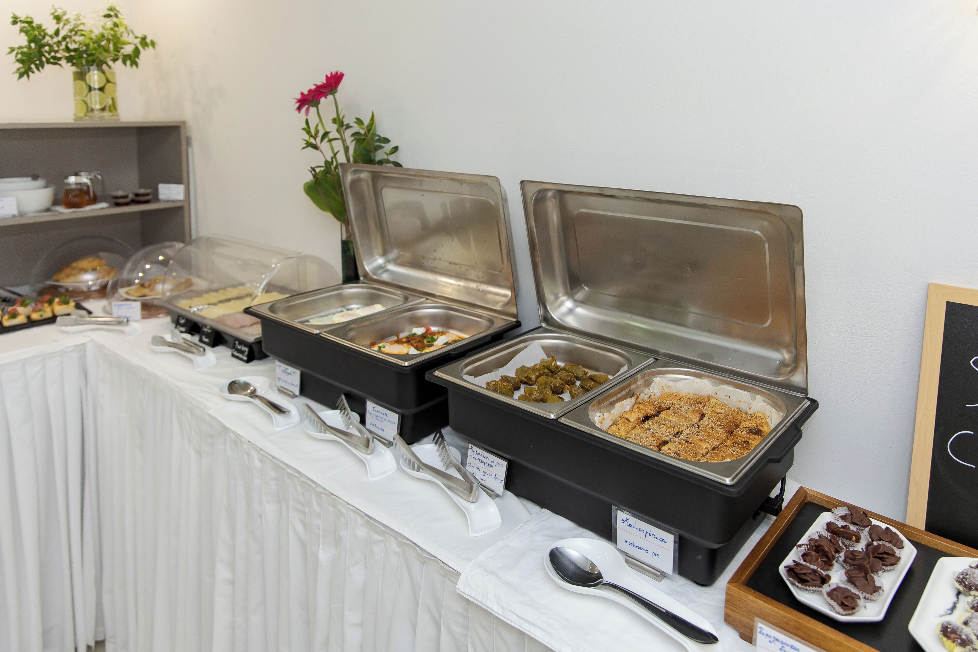 A buffet setup with various food items in clear containers, utensils, and a sign indicating 'Vegetarian'.