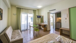 A hotel room with a bed, a sofa, a desk with a chair, a television, and a kitchenette. - Athina Beach Hotel (Chania)