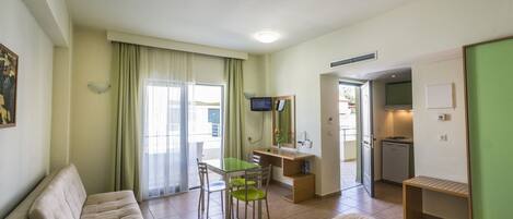 Ein Hotelzimmer mit einem Bett, einem Sofa, einem Schreibtisch mit Stuhl, einem Fernseher und einer Küchenzeile.