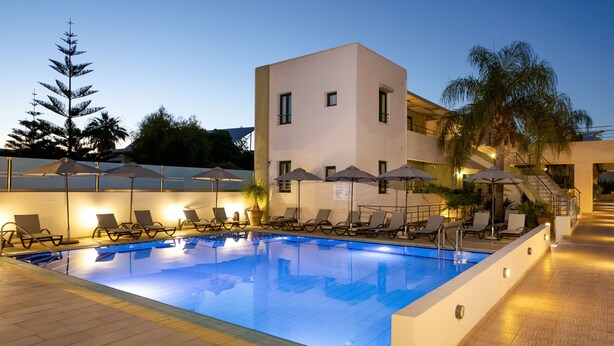 A swimming pool with lounge chairs and umbrellas, a modern building with a flat roof, and palm trees in the background. - Athina Beach Hotel (Chania)