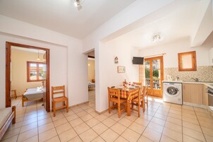 Ampla sala de estar com mesa de jantar, cadeiras, máquina de lavar e cozinha.