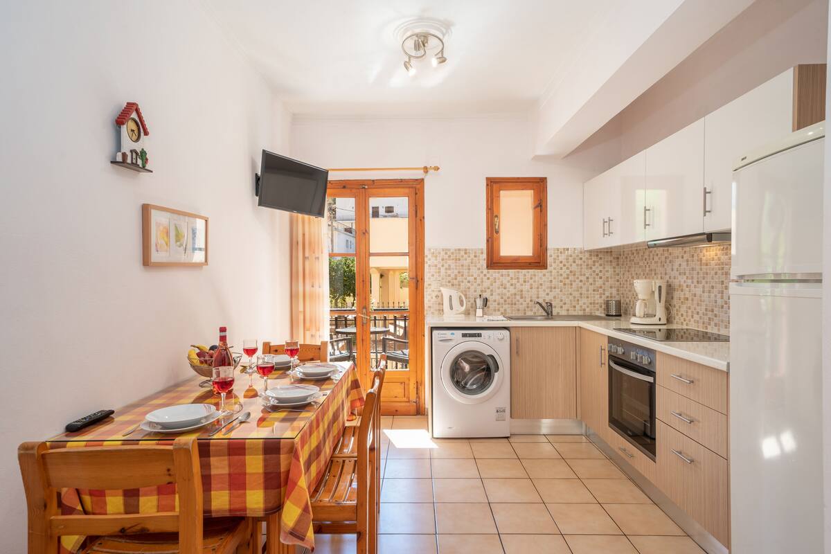 Una cocina compacta con lavadora, una mesa de comedor para dos personas y un televisor montado en la pared.