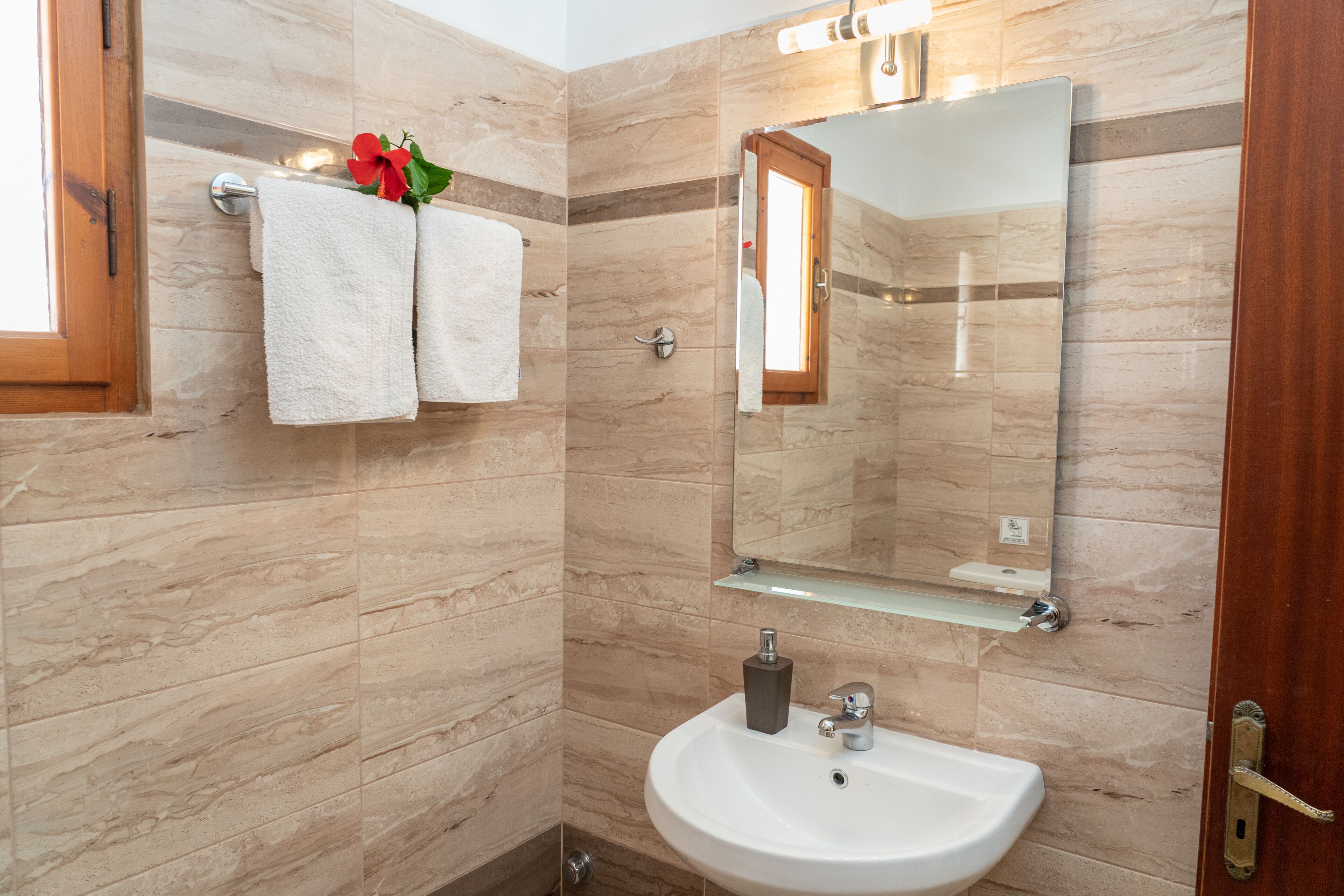 A bathroom with a marble wall, a sink, a mirror, and two towels.
