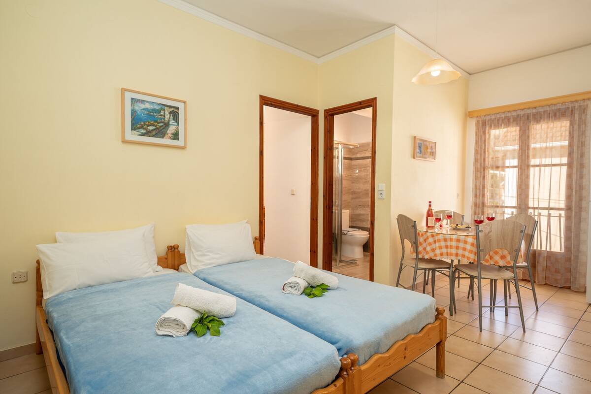 Una habitación con dos camas, una mesa de comedor con sillas y un baño visible a través de una puerta abierta.