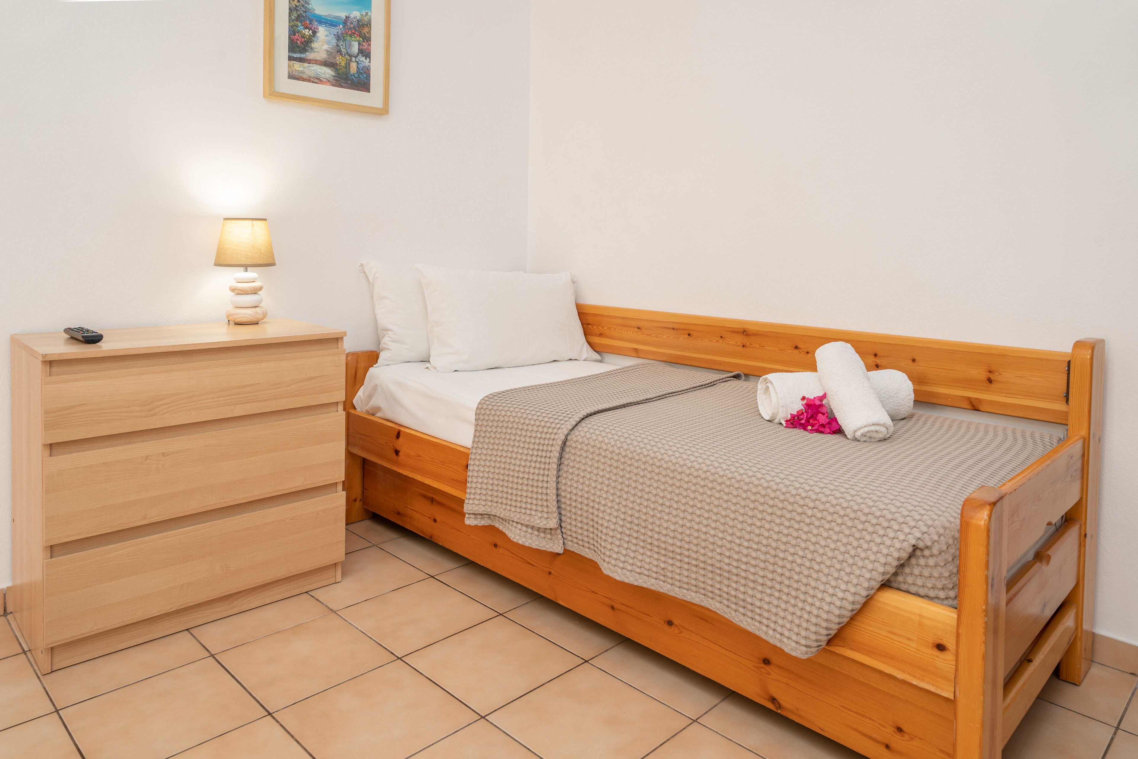 Une chambre à coucher bien rangée, avec un lit en bois, une table de chevet avec une lampe et une petite commode.