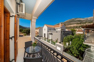 Uma varanda com mesa e cadeiras, com vista para uma área residencial com casas e uma montanha ao fundo.