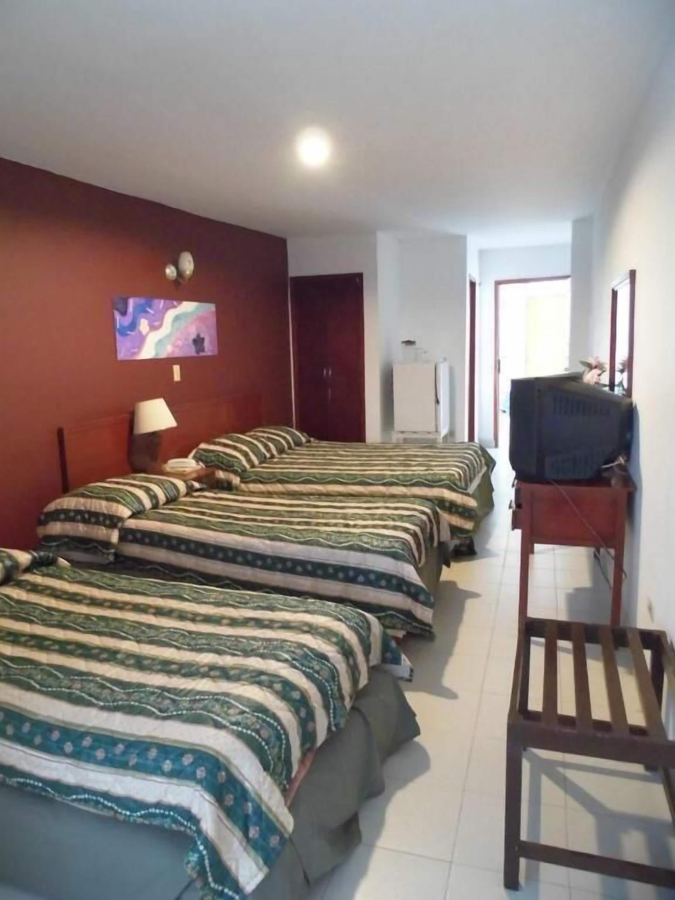 A hotel room with multiple beds, a television on a stand, and a door leading to another room.