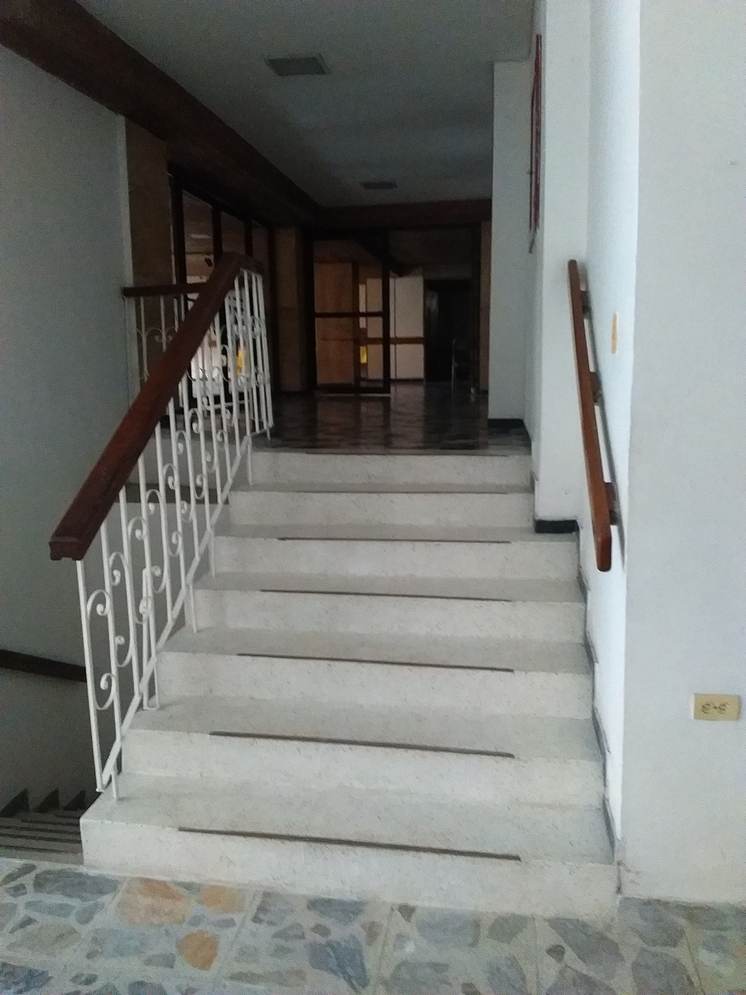 Una escalera con escalones blancos y barandilla de madera que conduce a una habitación con piso de baldosas.