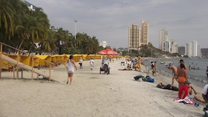 A beach with yellow canopies, palm trees, and people. - Hotel Betoma (Santa Marta)