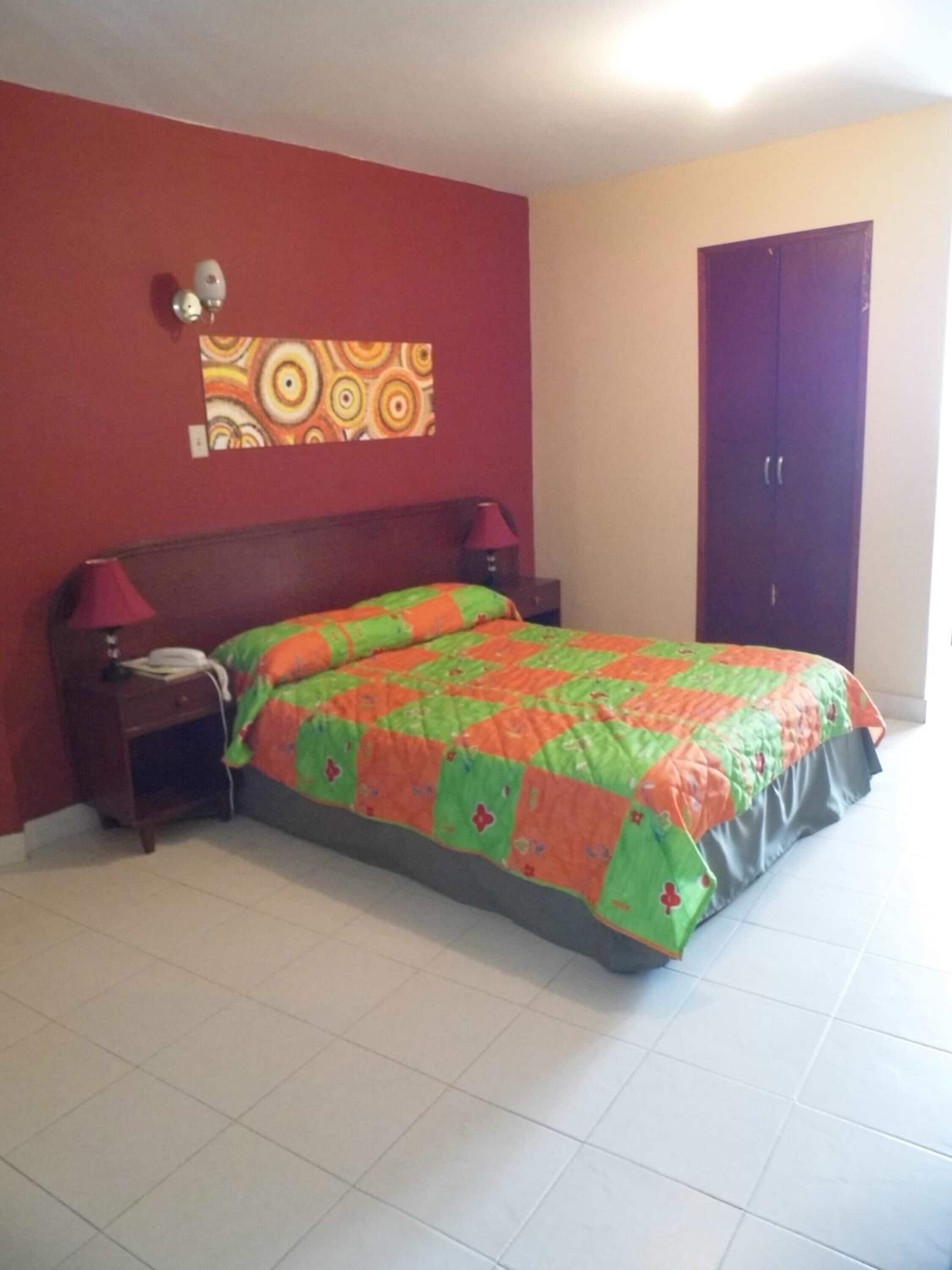 A bedroom with a bed, two bedside lamps, a nightstand, a wall clock, and a door.