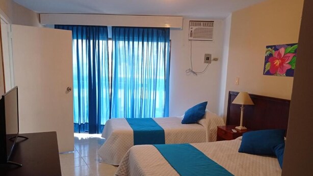A hotel room with two beds, a TV, a desk, and a window with curtains. - Hotel Betoma (Santa Marta)