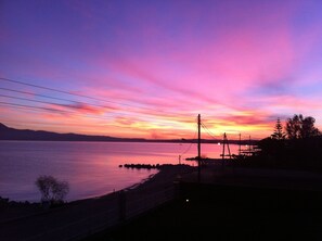 A sunset over a calm body of water with a distant shoreline, power lines, and a few trees. - Chris Studios & Apartments (Corinth)