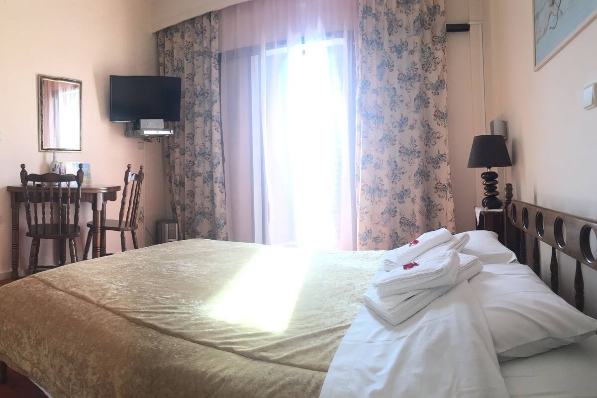 A hotel room with a bed, a desk, a chair, a television, and a window with curtains.