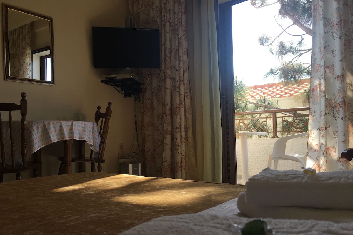 A hotel room with a bed, a TV mounted on the wall, a table with a striped tablecloth, and a chair.