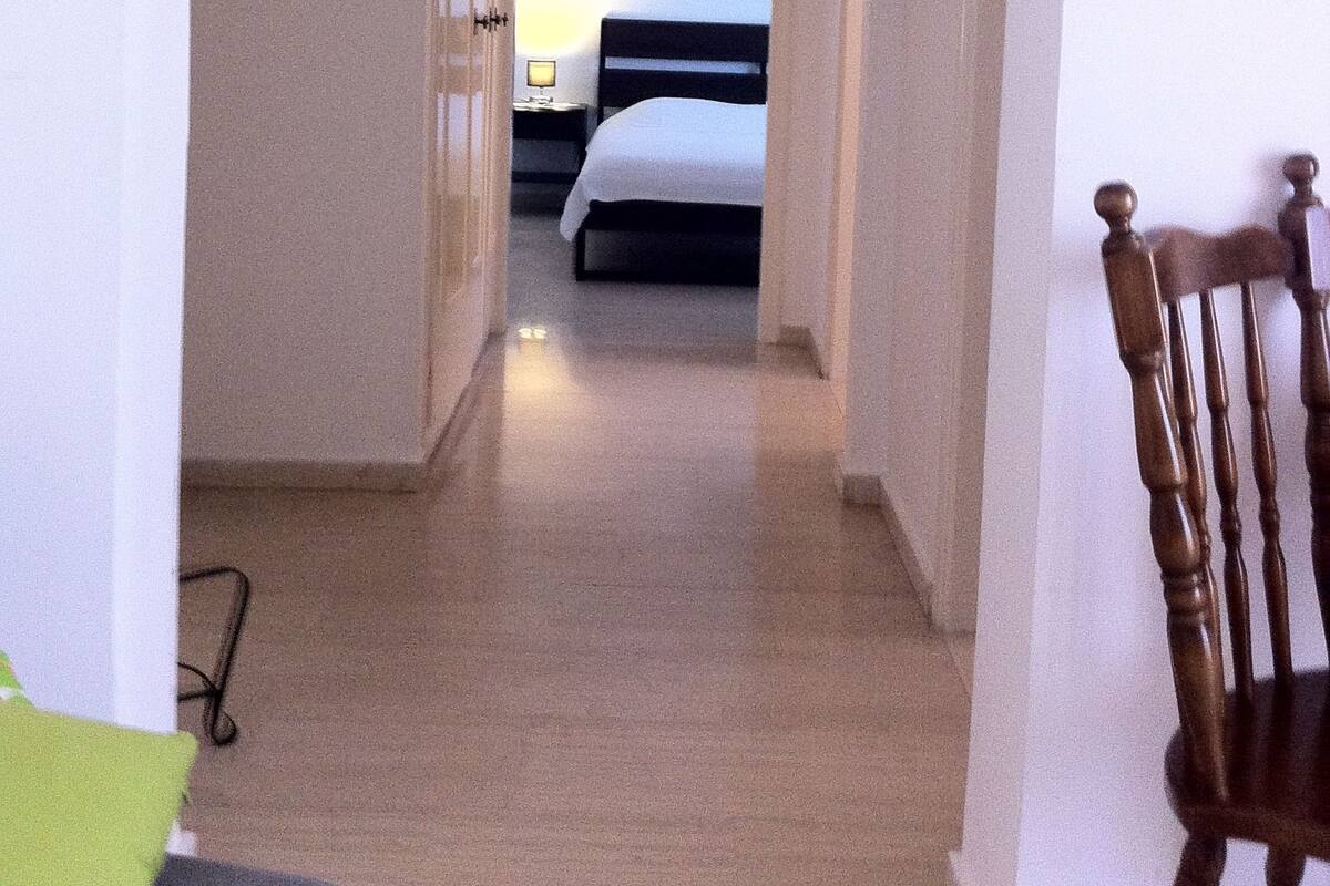 A hallway leading to a bedroom with a bed, a nightstand, and a lamp.