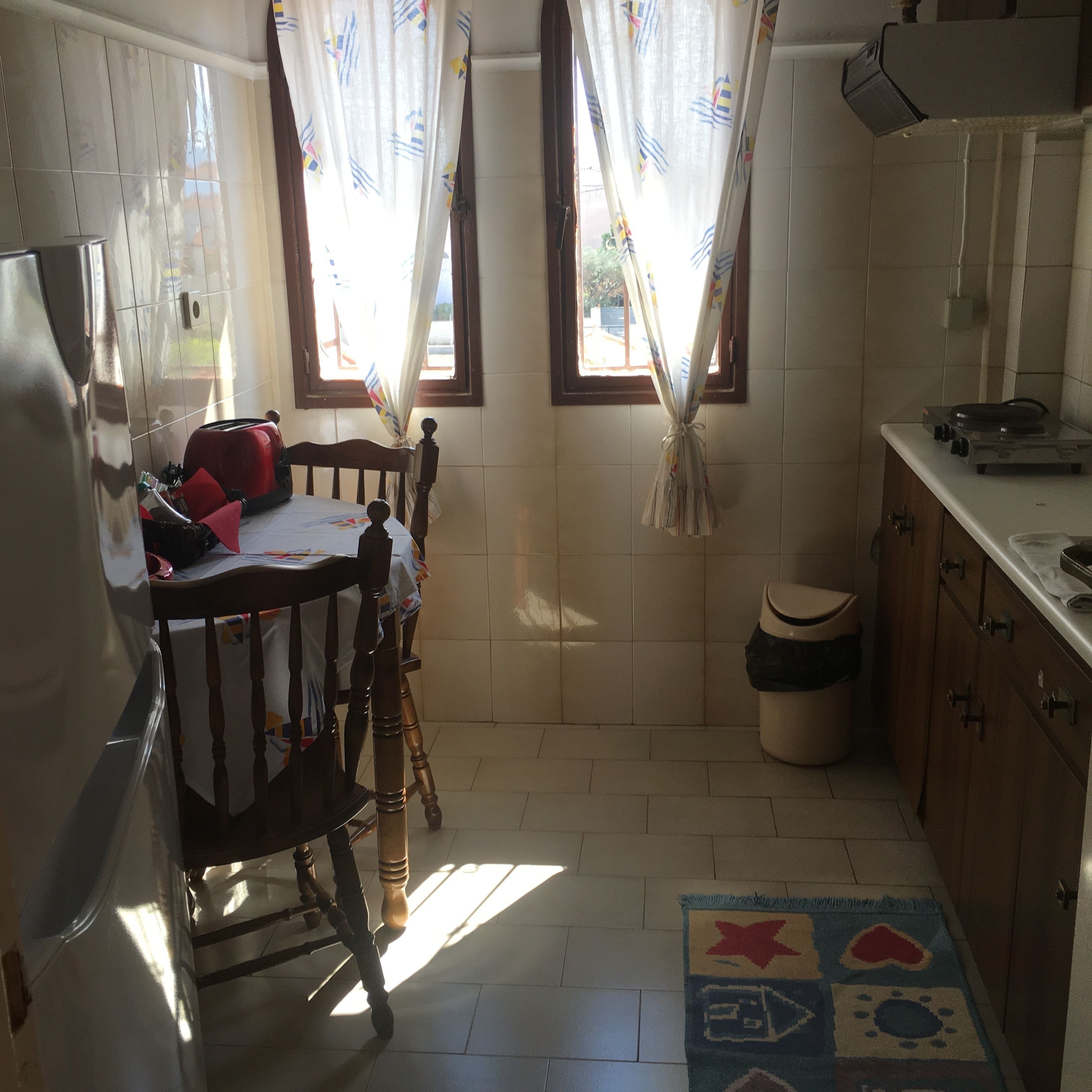 A compact kitchen with a dining area, a small trash bin, and a rug on the floor.