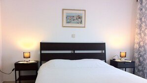 A neatly made bed with a white comforter in a room with a dark headboard. There are two bedside tables with lamps on either side of the bed. A framed picture hangs on the wall above the bed.