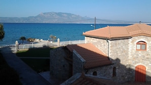 A stone building with a tiled roof, a white fence, and a view of the sea.