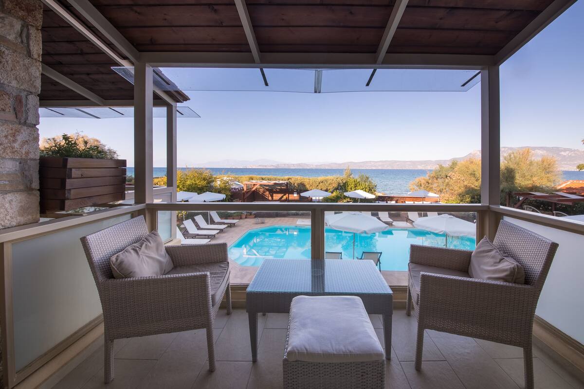 Ein Balkon mit Korbmöbeln, ein Schwimmbad und Meerblick.