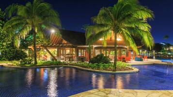 A pool area with a tiled edge, palm trees, and a building with outdoor seating.