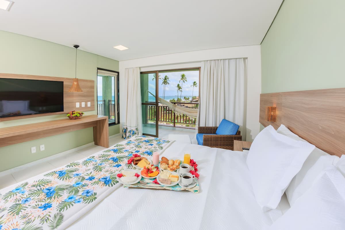 A hotel room with a bed, a TV, a breakfast tray, a balcony with a view of palm trees and the sea.