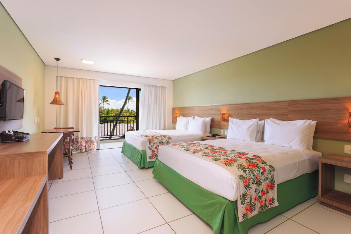 A hotel room with two beds, a desk, a chair, a television, and a balcony with a view of palm trees.