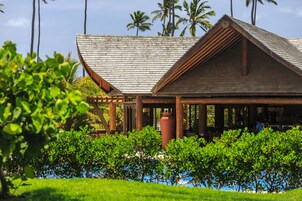 A wooden building with a sloped roof, surrounded by lush greenery and palm trees.