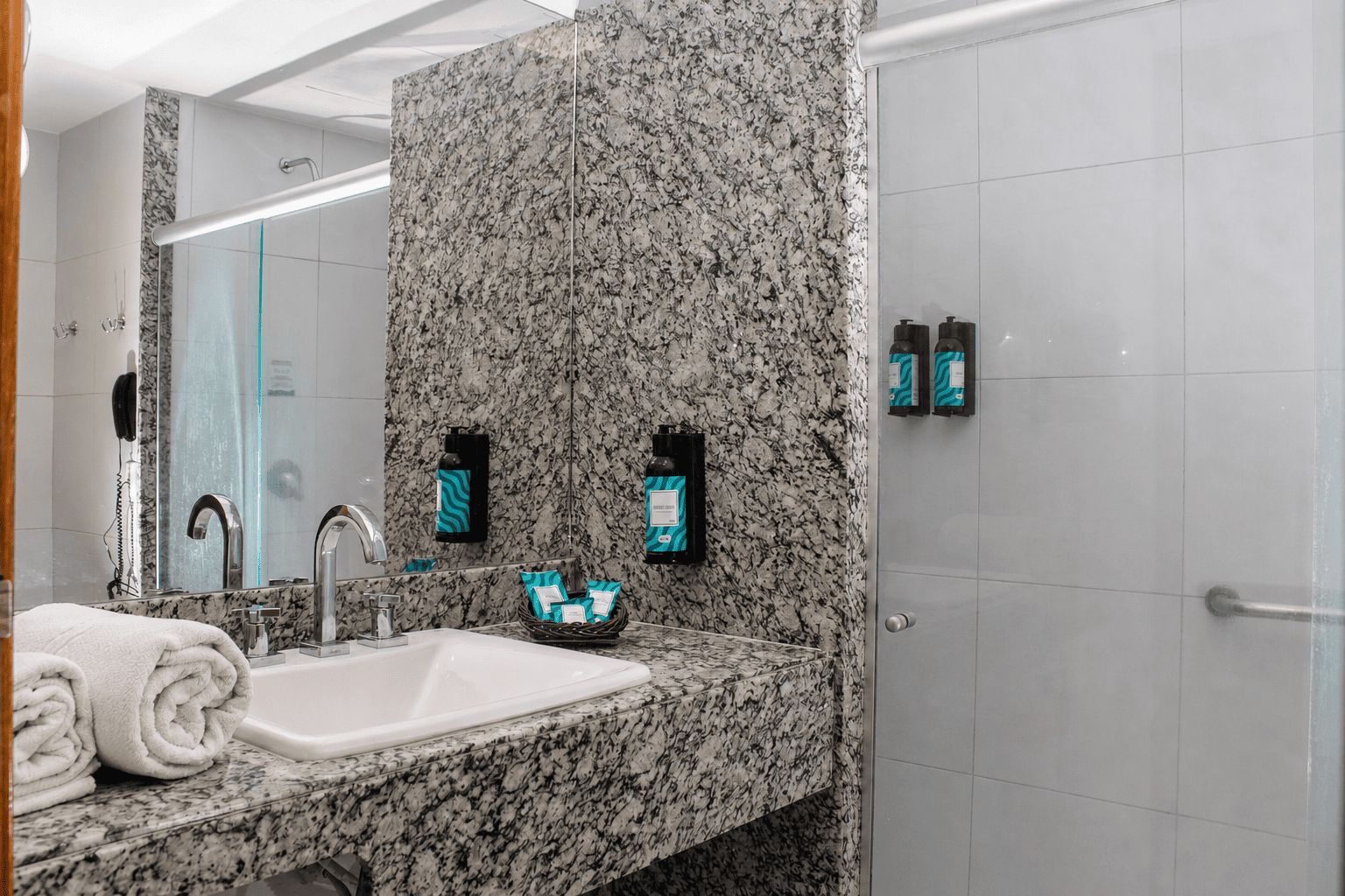 A modern bathroom with a granite countertop, a sink, a mirror, and a shower area.