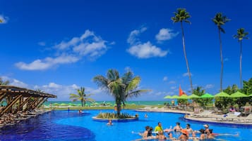 Relax by the pool surrounded by palm trees and lounge chairs, with a wooden deck and a small island in the center.