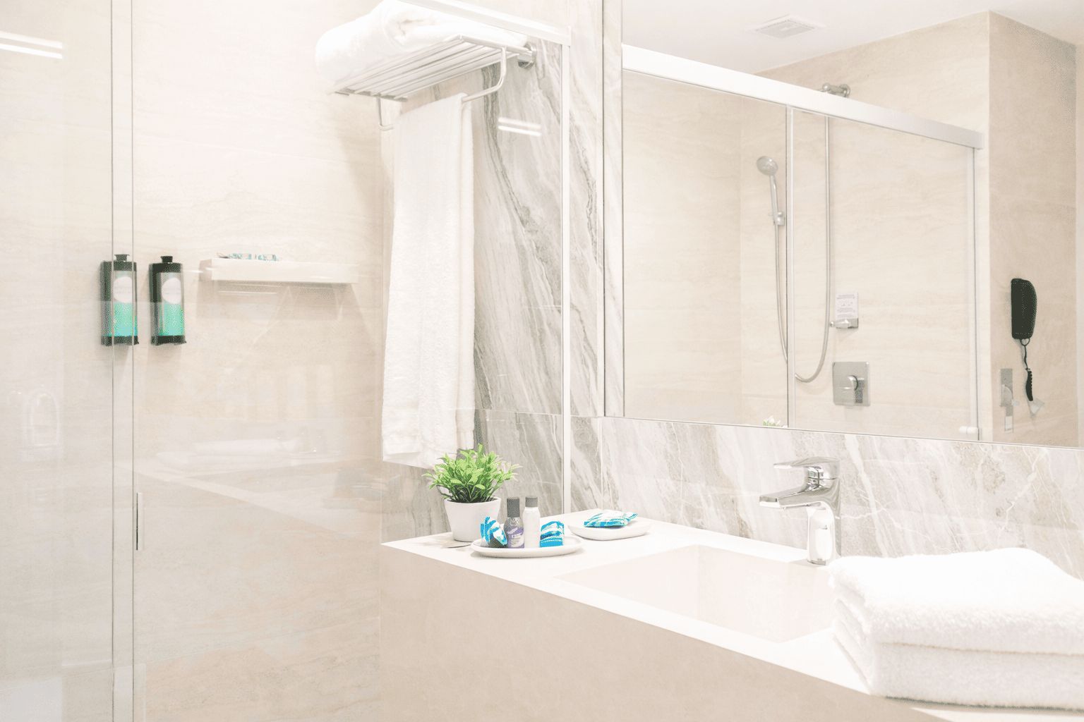 A modern bathroom with a glass shower enclosure, a marble countertop, a sink, a mirror, and a towel rack.