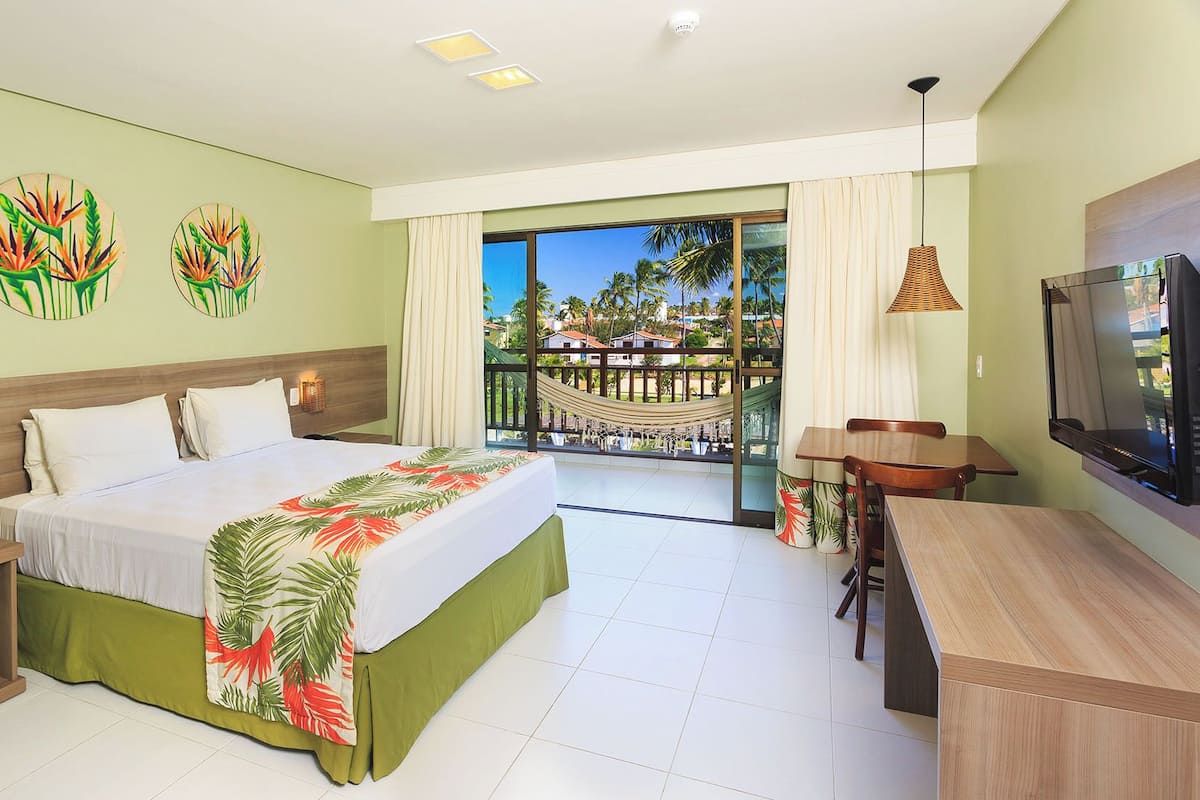 A hotel room with a bed, a desk, a TV, and a balcony with a view.