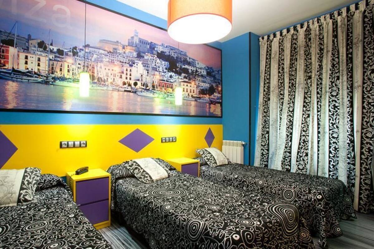 A hotel room with two beds, a large cityscape painting on the wall, and patterned curtains.